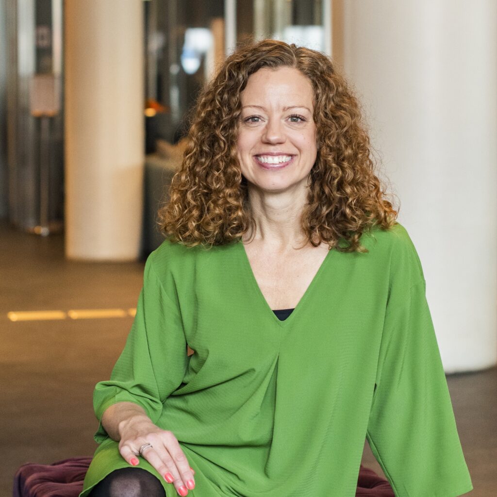 Anna Kleinwichs Magnusson sitter leende i en grön klänning och tittar rakt in i kameran.